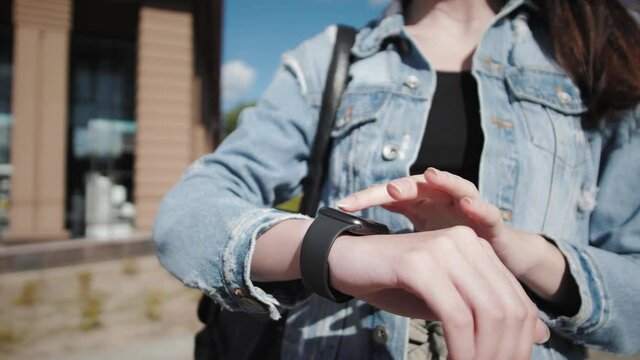 Girl Using Smart Watch Wearable Wristband Device. Touch Screen Wearable Technology Smart Band On Wrist Outdoor.Woman Scrolling On Display On Smart watch. Female Checking Pulse On Smart watch App.