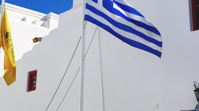 Bottom view of an Orthodox church in Mykonos against blue sky with waving Greek flag and other colorful pennants
