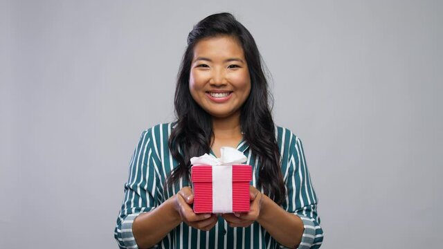 birthday present, surprise and people concept - happy smiling young asian woman holding gift box over grey background