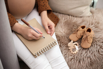 Pregnant woman writing baby names list at home, closeup