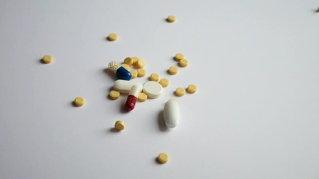 A hand pours different pills and capsules onto a white surface close up