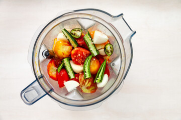 Blender cup with ripe cut tomatoes, green chili, garlic and salt to make fast tomato sauce. Top view of plastic mixer cup.