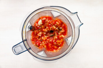 Blender cup with smashed tomatoes and other vegetables. Fast tomato sauce. Top view of plastic mixer cup.