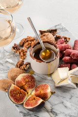 Brie and cheese with paprika, salami, figs, walnuts, honey and rose wine on a marble board. Food for a romantic date on a light concrete background. Top view