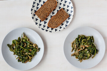 Curly endive (Cichorium endivia)stir-fry dish with garlic on two plates and two bread slices on triangle patterned plate top view.