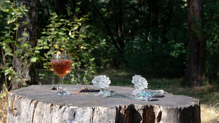 A glass of rose wine and two wonderful vintage  crystal roses as decoration are on the old stump.  The glass wine  wine  is lighted  by sunlight against the background of a dark wet forest.