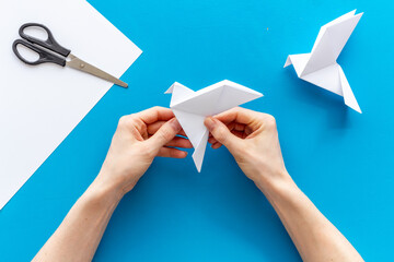 Female hands folding sheet of paper - origami bird. Overhead view