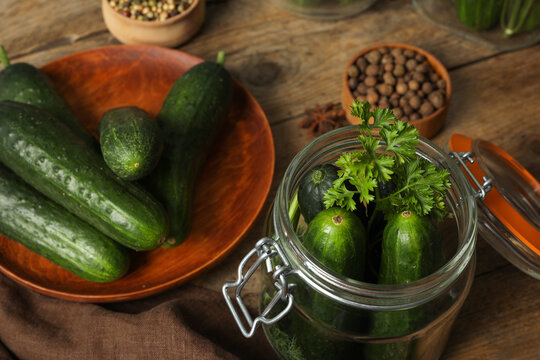 Pickling jar with fresh ripe cucumbers and spices on wooden table, closeup