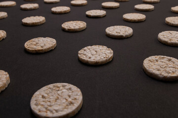 Fototapeta na wymiar Pattern distribution of rice crackers. Round rice crackers, spread out on a black background. Front or perspective design. Low key photography.