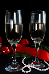Two glasses of champagne on the festive table on a dark background. next to Christmas decor red balls, ribbon, beads. Christmas composition. Selective focus