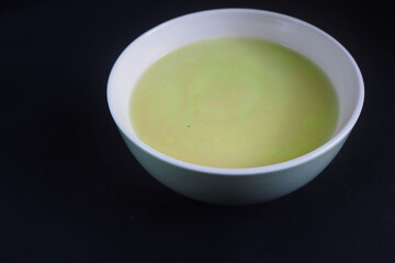 green and white plate with cream soup of zucchini, potatoes, cream, onions on a black background side view . cooking gluten-free food at home