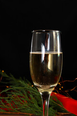 One glass of champagne on a dark background. festive composition with bright Christmas decoration, red ribbon, garland, Christmas tree. greeting card option.