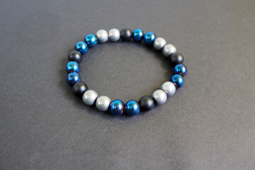 bracelet made of round natural stones made of black matte onyx and gray and blue hematite . men's bracelet on a black background side view