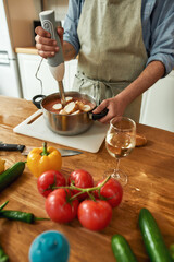 Cropped shot of man, chef cook using hand blender, blending chopped vegetables and bread while preparing Italian meal in the kitchen