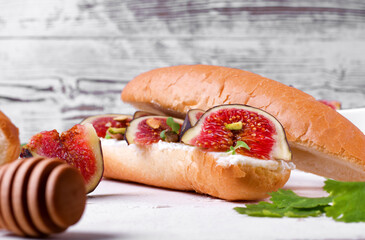 Sandwich with figs, cream cheese, pistachio nuts, microgreen and honey on the white table