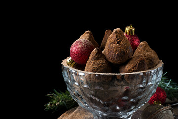 Chocolate truffles covered in cacao powder and red baubles against the black background. Christmas dessert