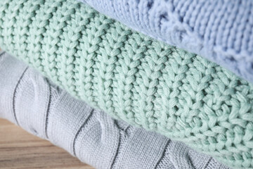 Stack of folded warm sweaters on wooden table, closeup