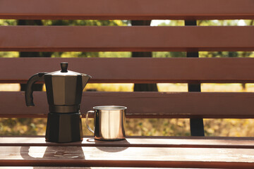 Coffee maker and metal cup on bench outdoor