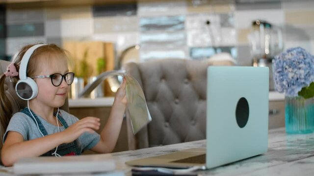 little girl shows homework notebook to online tutor in video call Rbbro. pupil wear headphones during distant learning and talk. concept e-learning, teacher, education. elementary student