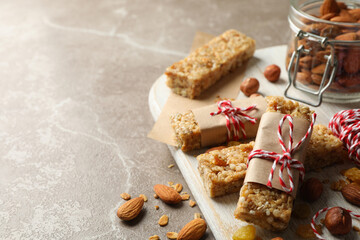 Fototapeta premium Board with tasty granola bars and nuts on gray background, space for text