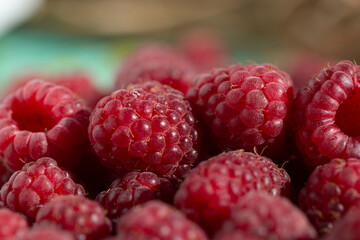 Juicy red raspberries lie in a pile on a blurry background