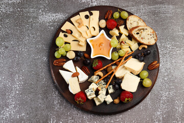 Сheese board served with honey, grapes, berries and nuts on a dark background. Top view, flat lay