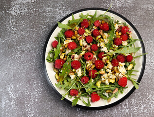 Arugula salad with raspberries and gorgonzola on a white rectangular plate on a dark background. Top view, flat lay
