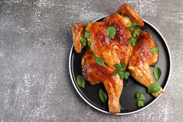 Baked whole chicken on a round plate on a dark background. Top view, flat lay