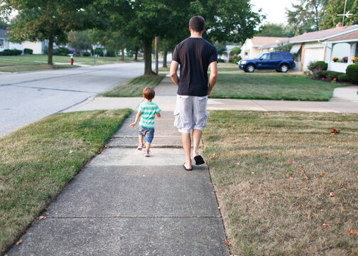 father and son walk down sidewalk