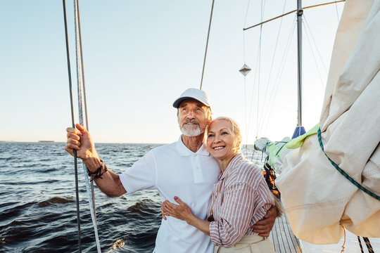 Loving senior couple enjoying vacation and looking to the distance. Mature couple standing together and embracing on a private sailboat.