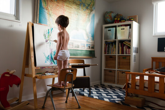 boy stands on chair to paint