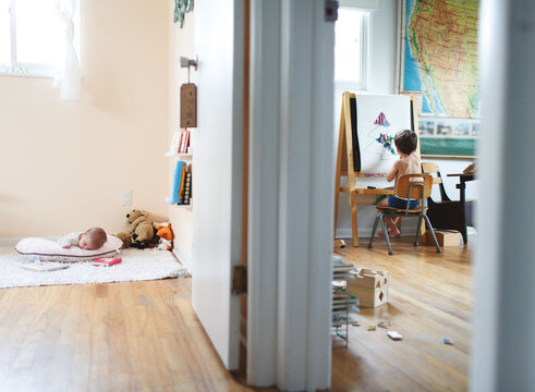 child paints at easel while baby sleeps in next room