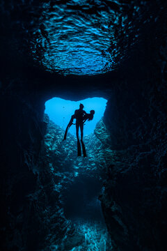 A male free diver carrying female in his arms in the cave with sun rays