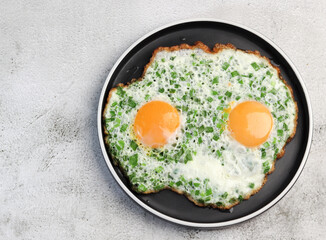 Fried eggs with green onions on a round plate on a light gray background. Top view, flat lay