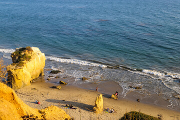 a shot of the deep blue ocean and the waves rolling into the beach with people relaxing on the...
