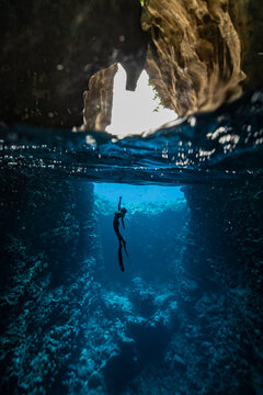 A female freediver with bikini and fins diving in the cave with sun rays
