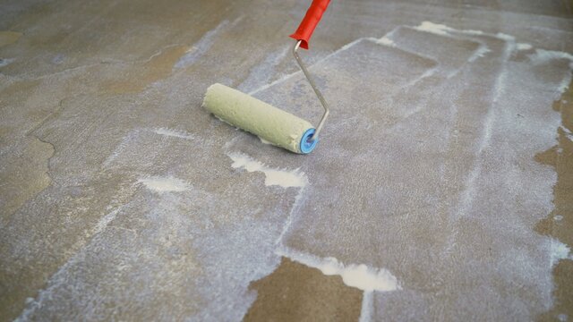 Priming the concrete floor with a roller. Professional floor primer. Leveling concrete floors. Floor repair using a primer.