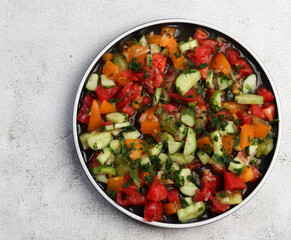 Cucumber, tomato and greens salad on a round plate on a light gray background. Top view, flat lay