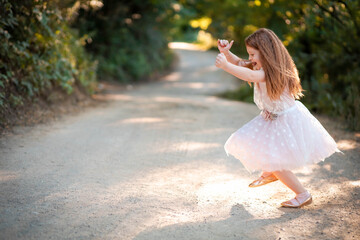 Little redhead in white dress jumps on the road, looking very happy