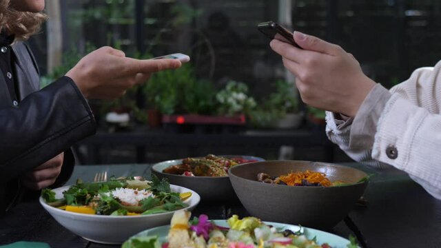 Two pair of hands taking pictures of healthy vegan meals served on black wooden table