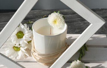 Fototapeta na wymiar Organic scented soy candle on white wooden rack. white frame. Loft interior decor, minimalism concept. Closeup view, flower design.