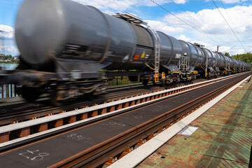 Fototapeta na wymiar Blurry photo of railroad tank cars in motion, on a metal bridge over the river.