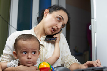 Mommy talking on the phone. Working from home due to coronavirus. A young middle-eastern woman trying to work at home while sitting with her baby boy