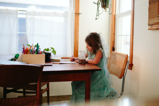 little girl sits and table and writes