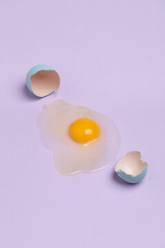 Broken blue colored egg with yolk on pastel background