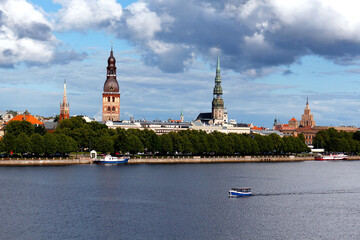 Fototapeta premium Beautiful panoramic view of the old town of Riga, Latvia. Amazing cityscape with clouds and a boat floating on the river.