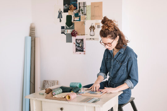 Focused Young Woman Choosing Color Sample For Moodboard On Wooden Table