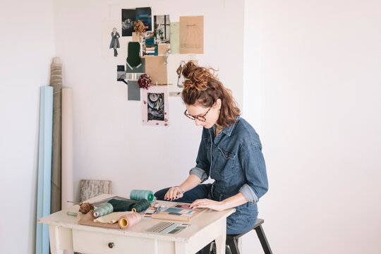 Focused Young Woman Choosing Color Sample For Moodboard On Wooden Table