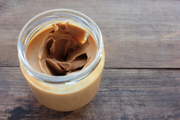 Peanut butter jar on wooden table background. Healthy snacks for kids. Top view, copy space