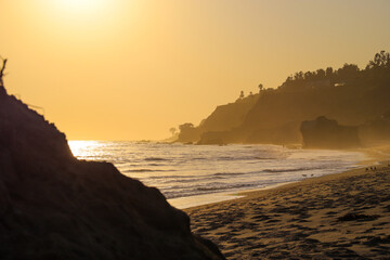 a stunning shot of the sunset and the ocean and the rock and people walking on the beach at El...